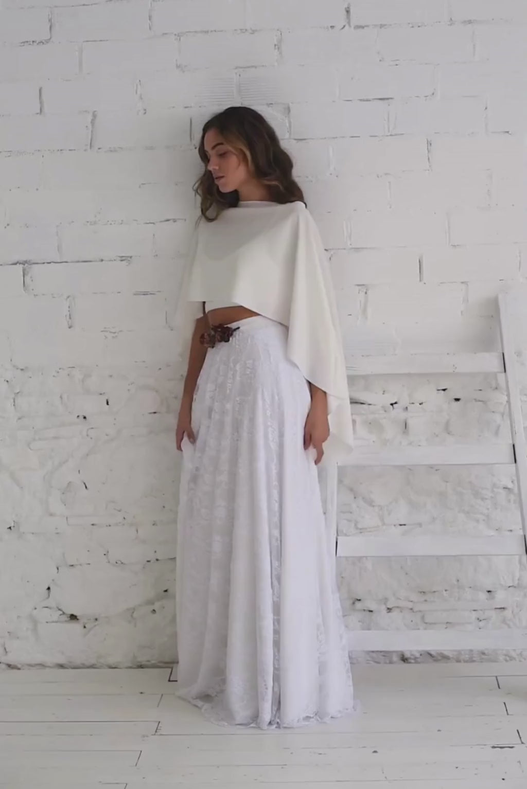 Video de modelo de perfil apoyada a la pared y andando a cámara con vestido de novia con capa corta.