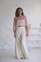 Video de modelo con capa de tela de encaje de cuarzo rosa y pantalon palazzo blanco con tube top blanco