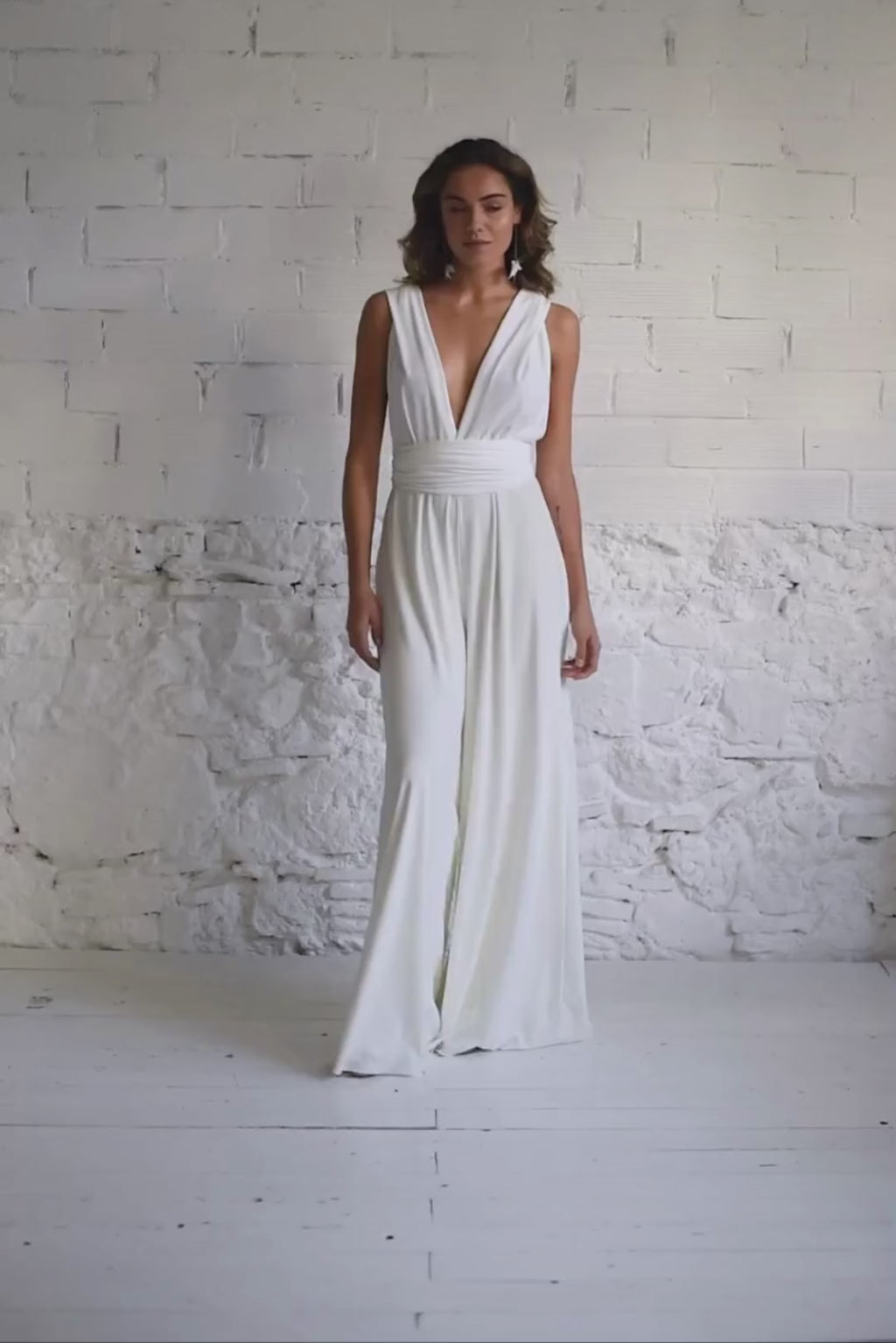 Video de modelo andando a cámara con mono de novia pantalón con escote en V y espalda con lazos en cruz.