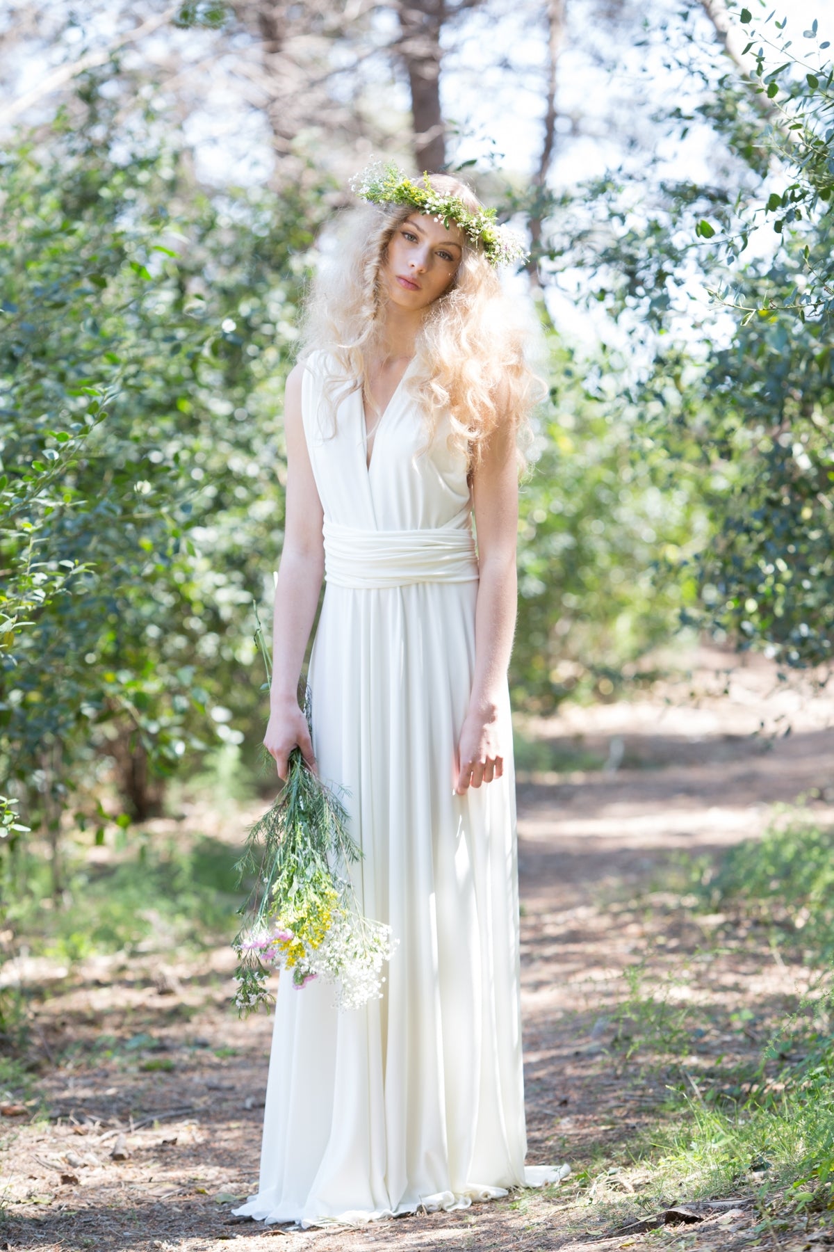 Mujer vistiendo un vestido de novia largo en color crudo, complementado con un romántico ramo de flores y una corona floral