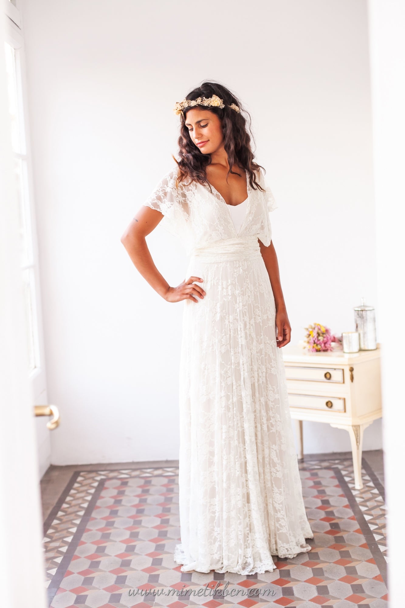 Modelo luciendo un elegante vestido de novia blanco con sobrevestido de encaje, destacando la delicada cintura elástica y el toque romántico