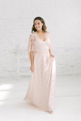 Modelo sujetando vestido con mano izquierda y andando hacia la camara. Vestido de novia de encaje rosa cuarzo.