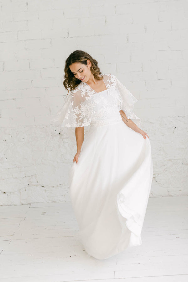 modelo chica moviendo la falda de su vestido de novia dos piezas compuesto por: falda en crepe elástico + top Lily de capa corta en tela de encaje de flores blancas.