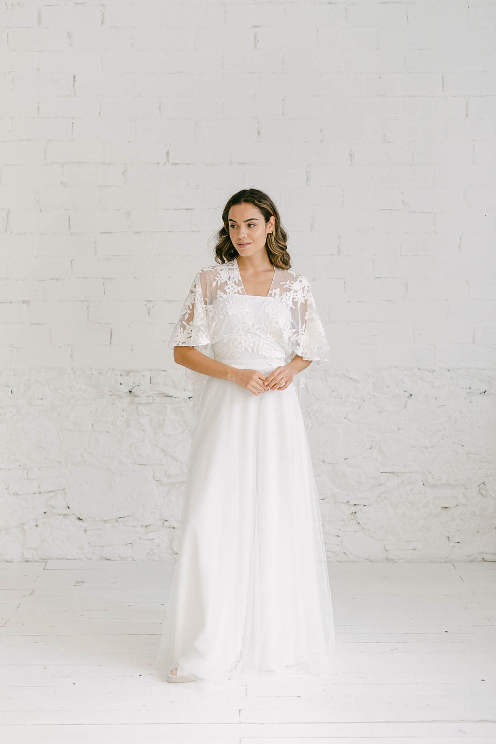 Modelo cchica con vestido de novia dos piezas blanco con top de capa corta en tela de encaje blanco.