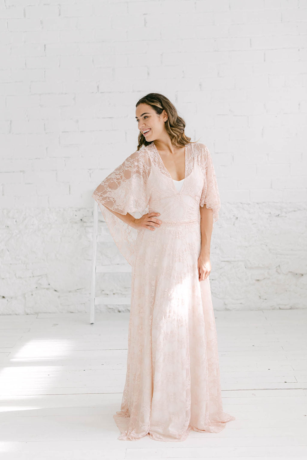 Modelo sonriendo hacia la derecha con vestido de boda dos piezas en tela de encaje rosa palo.