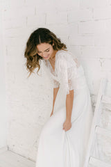 Modelo apoyada en pared blanca con vestido de novia de encaje dos piezas.